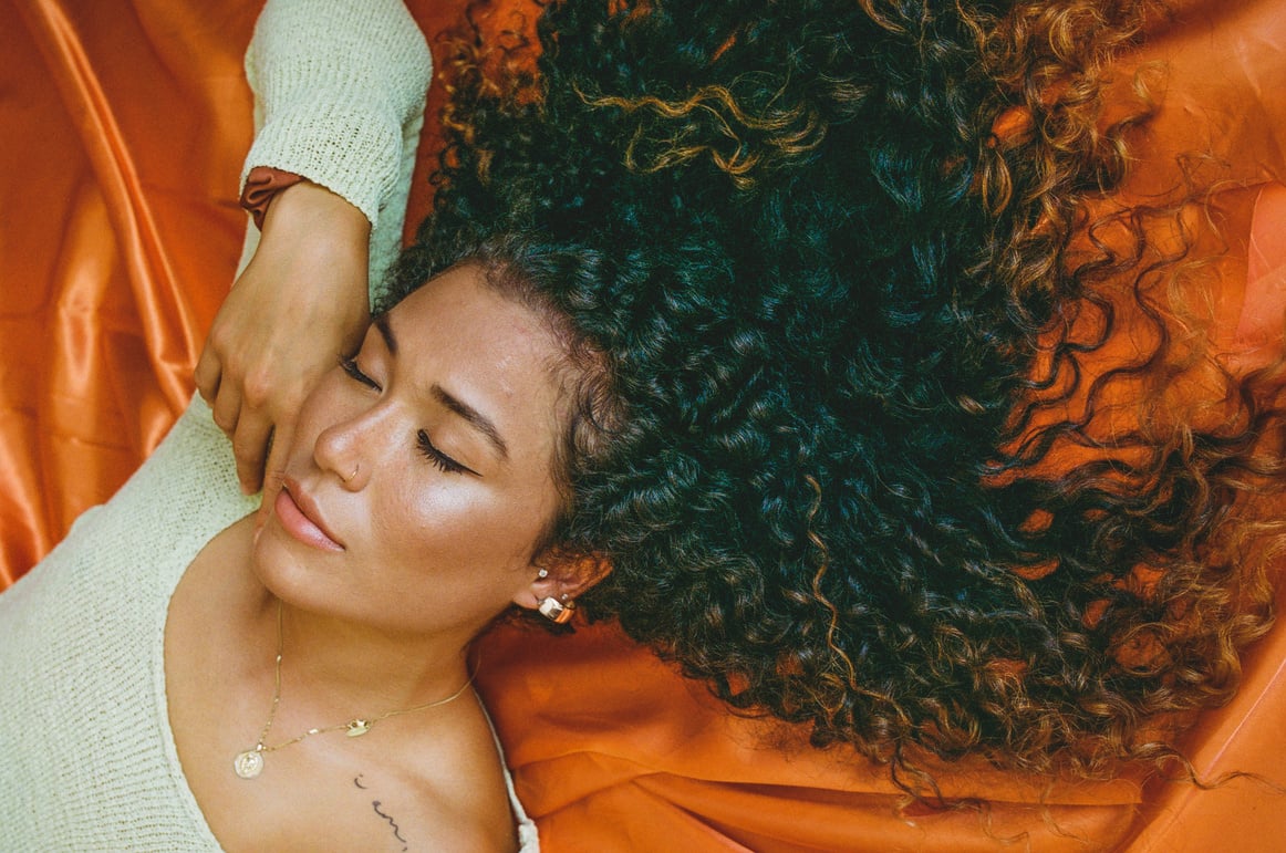 Woman with Curly Hair Lying on Orange Fabric